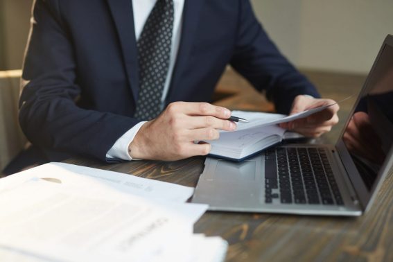 Closeup portrait d'un homme d'affaires prospère méconnaissable analysant des documents contractuels au bureau avec un ordinateur portable